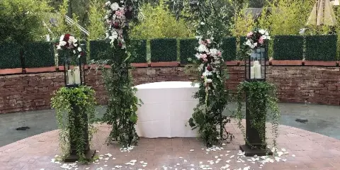 Outdoor wedding ceremony setup featuring a floral arch, white altar table, and pedestals with candles and flowers.