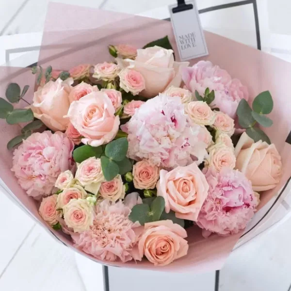 A wrapped bouquet of pink roses and carnations with eucalyptus leaves