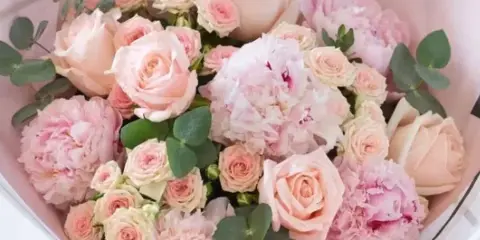 A wrapped bouquet of pink roses and carnations with eucalyptus leaves