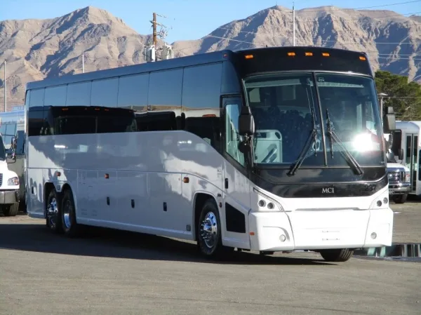 A white and black MCI charter coach bus parked in a lot with mountains in the background.