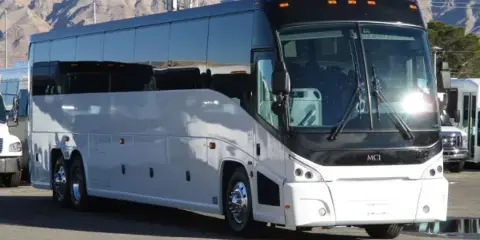 A white and black MCI charter coach bus parked in a lot with mountains in the background.