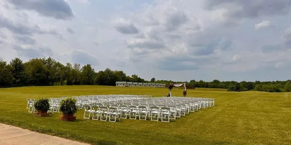 Outdoor wedding ceremony setup with white chairs and an arch on a grassy field.