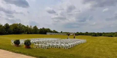 Outdoor wedding ceremony setup with white chairs and an arch on a grassy field.