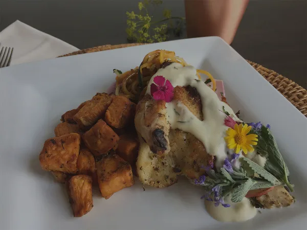 A plated meal featuring roasted potatoes and a protein dish with cream sauce and edible flower garnishes on a white square plate.