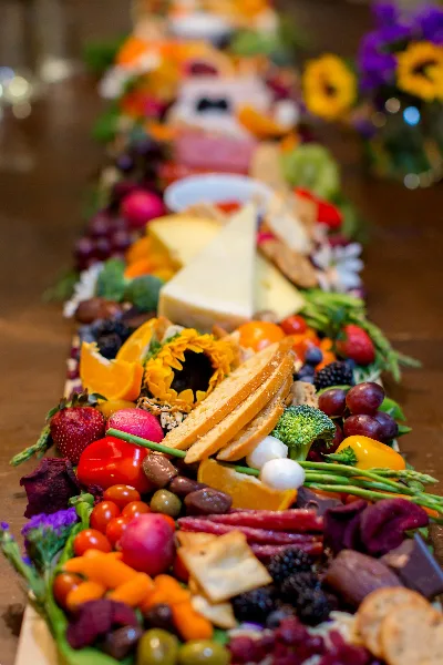 A long, elaborately styled grazing table filled with colorful fruits, vegetables, cheeses, meats, and breads.
