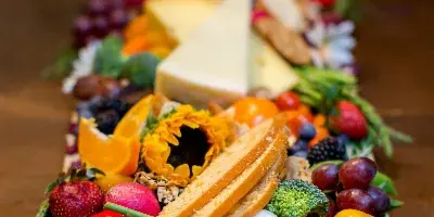 A long, elaborately styled grazing table filled with colorful fruits, vegetables, cheeses, meats, and breads.