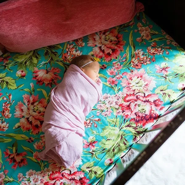 A newborn baby wrapped in a pink blanket sleeping on a floral patterned surface.