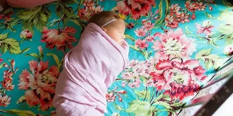 A newborn baby wrapped in a pink blanket sleeping on a floral patterned surface.