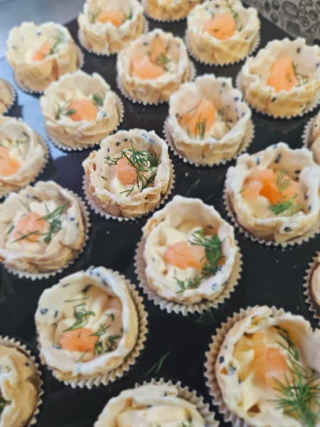 A tray of individual appetizer tartlets topped with cream cheese, salmon, and fresh dill.