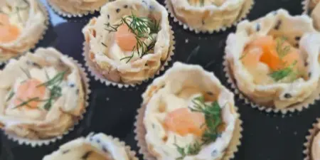 A tray of individual appetizer tartlets topped with cream cheese, salmon, and fresh dill.