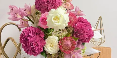 A floral arrangement with pink and white flowers in a white bucket, with a Poppy Flower Co. sign in the background.