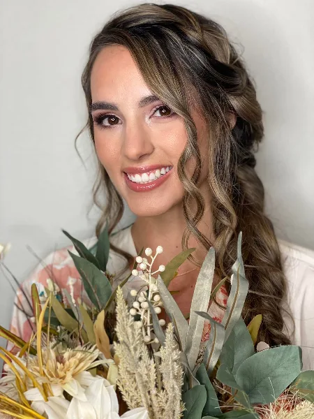 Bride with styled braided hair and makeup holding a floral bouquet