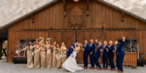 A wedding party posing in front of a large wooden barn structure.