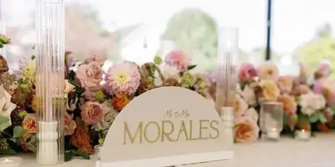 A personalized lettered wedding sign reading 'MORALES' displayed on a table with floral arrangements and tall glass candle holders.