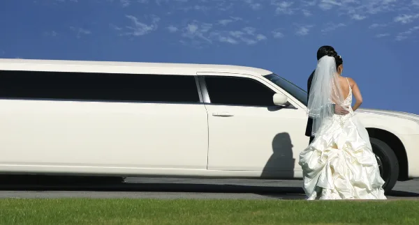 A bride and groom standing beside a white stretch limousine outdoors.
