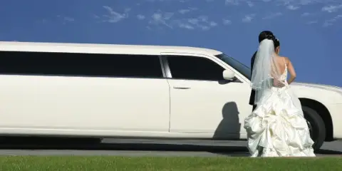 A bride and groom standing beside a white stretch limousine outdoors.