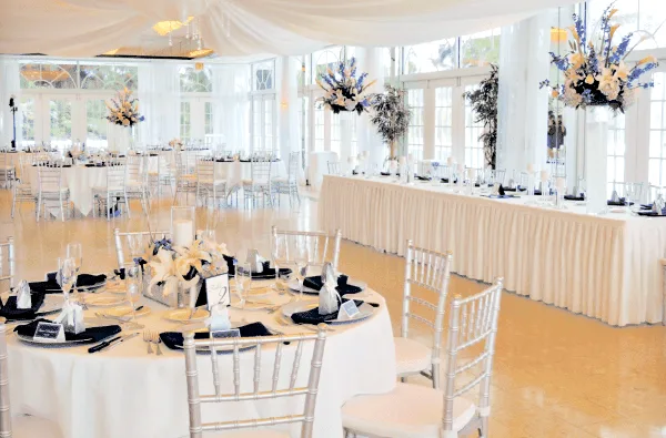 An elegant event space set up with round tables, white linens, silver Chiavari chairs, and floral centerpieces.