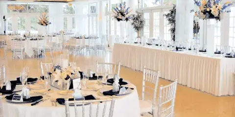 An elegant event space set up with round tables, white linens, silver Chiavari chairs, and floral centerpieces.
