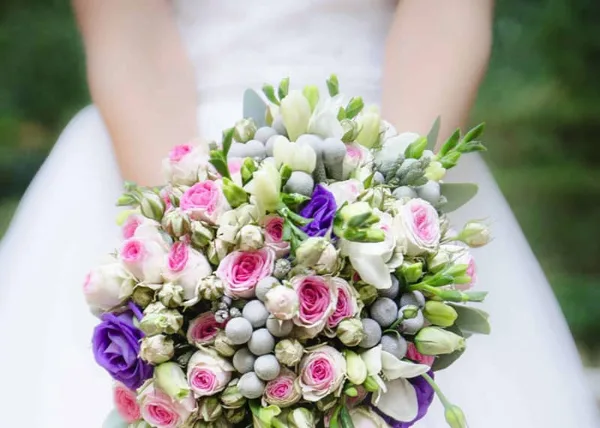 A close-up of a bride holding a large, round wedding bouquet featuring pink roses, white calla lilies, and greenery.