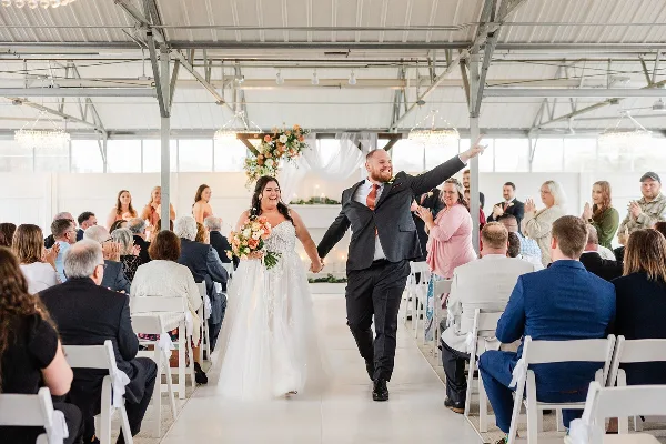 A bride and groom walking down the aisle during a wedding reception in a large indoor venue with guests seated on either side.