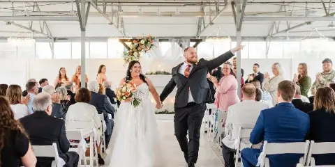 A bride and groom walking down the aisle during a wedding reception in a large indoor venue with guests seated on either side.
