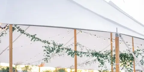 A white wedding tent interior with round tables, floral centerpieces, and hanging greenery.