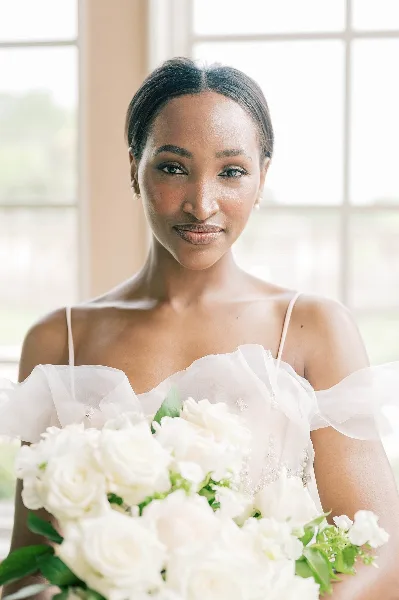 Portrait of a bride in a white gown holding a bouquet of white roses.