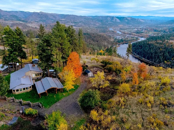 Aerial view of a rural property with a house and outbuildings overlooking a river valley and mountains.