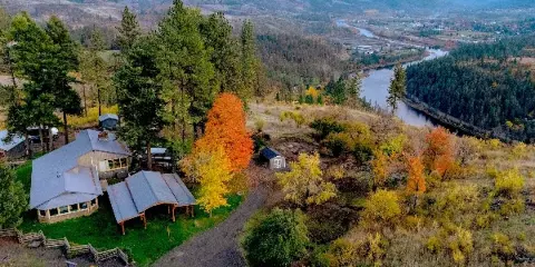 Aerial view of a rural property with a house and outbuildings overlooking a river valley and mountains.
