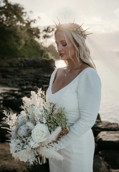 A bride with styled hair and makeup holding a bouquet outdoors.