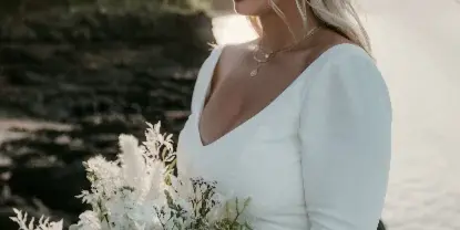 A bride with styled hair and makeup holding a bouquet outdoors.