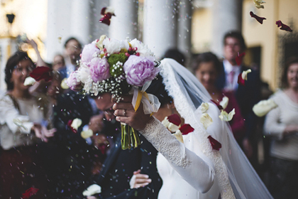 A bride and groom exiting a vehicle while guests throw flower petals.