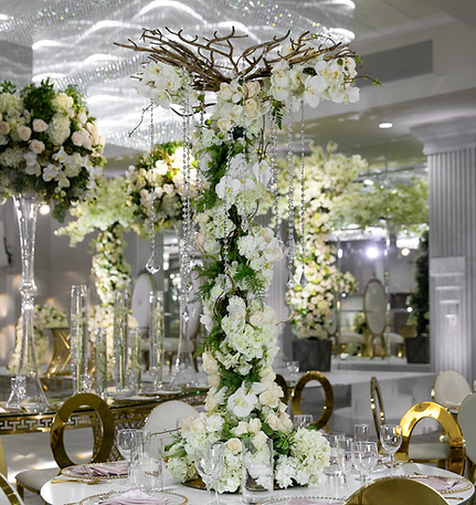 A tall, elegant floral centerpiece with white flowers and greenery on a decorated table.