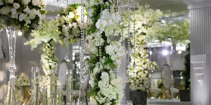A tall, elegant floral centerpiece with white flowers and greenery on a decorated table.
