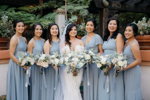A bride and her bridesmaids in matching blue dresses holding bouquets.