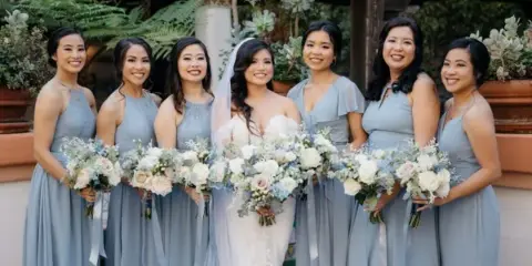 A bride and her bridesmaids in matching blue dresses holding bouquets.
