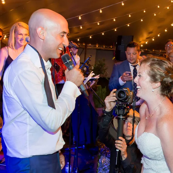 A live band member singing into a microphone while interacting with a bride at a wedding reception.
