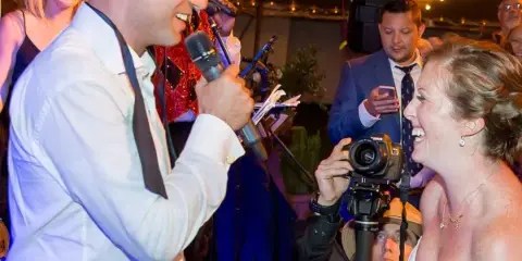 A live band member singing into a microphone while interacting with a bride at a wedding reception.