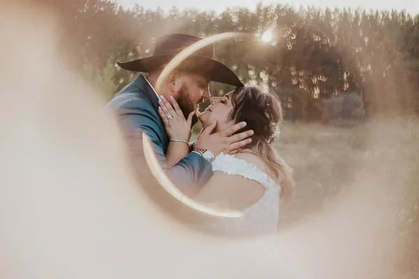 A wedding couple embracing in a field with a lens flare effect.