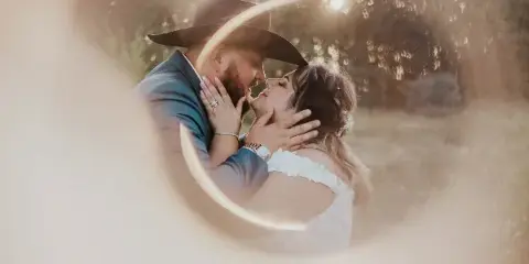 A wedding couple embracing in a field with a lens flare effect.