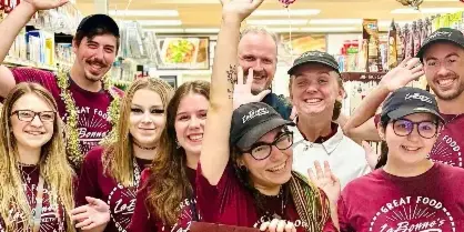 A group of smiling LaBonne's Markets employees wearing maroon branded shirts and caps, posing together in a grocery store aisle.