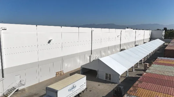 Aerial view of a large white commercial event tent set up next to a warehouse, with a Funtastic Rentals delivery trailer in the foreground.