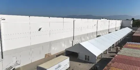 Aerial view of a large white commercial event tent set up next to a warehouse, with a Funtastic Rentals delivery trailer in the foreground.