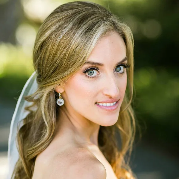 A bride with styled blonde hair and airbrush makeup wearing a veil and earrings.