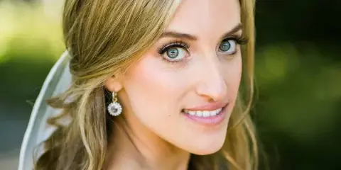 A bride with styled blonde hair and airbrush makeup wearing a veil and earrings.