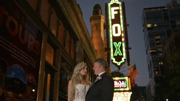 A bride and groom standing together in front of the illuminated Fox Theatre sign at dusk.