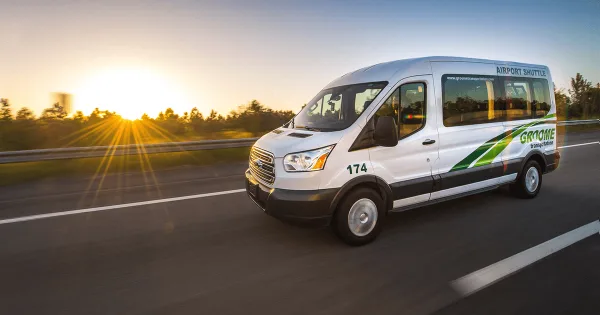 A white Groome Transportation shuttle van driving on a highway at sunset.