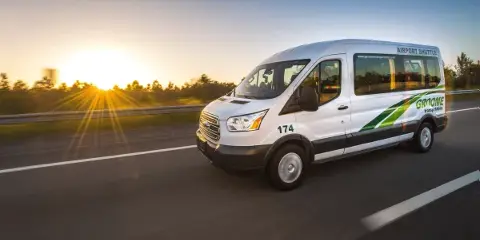 A white Groome Transportation shuttle van driving on a highway at sunset.