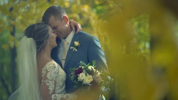 A cinematic wedding video still showing a bride and groom embracing outdoors with a soft, golden-hour background.