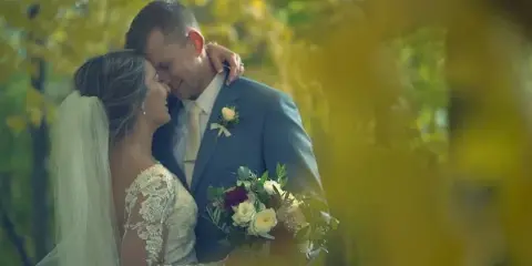 A cinematic wedding video still showing a bride and groom embracing outdoors with a soft, golden-hour background.